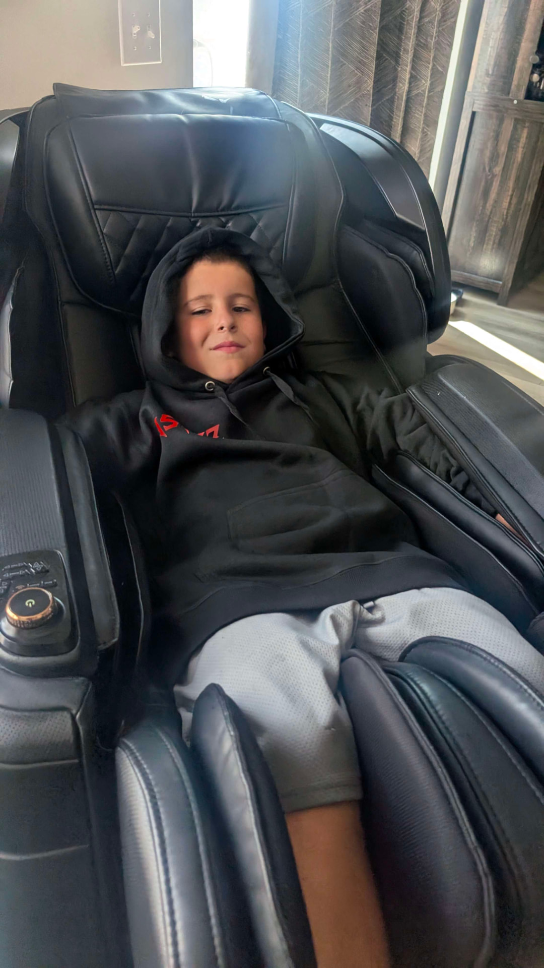Ollie relaxing in a massage chair wearing a black hoodie